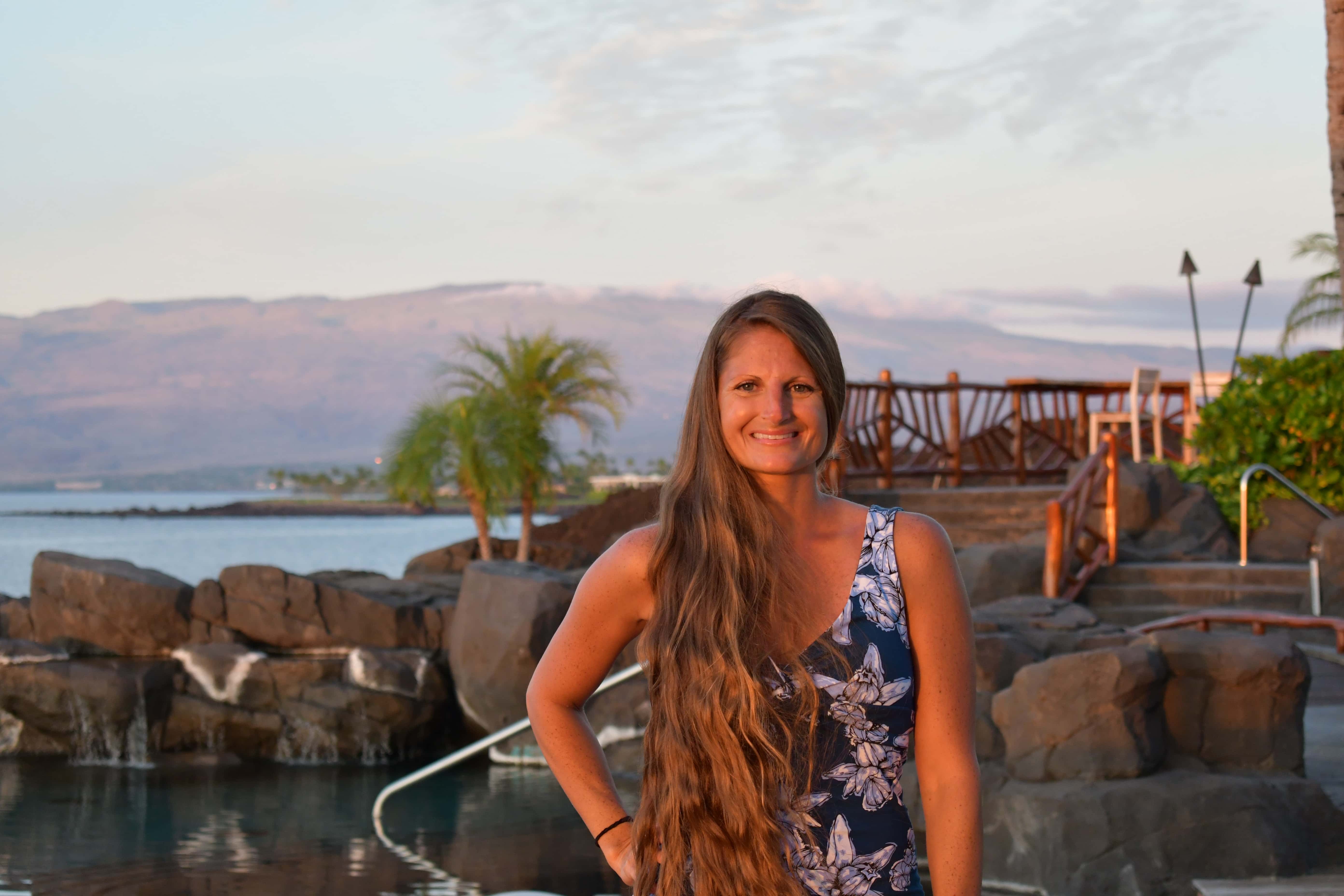 woman with long hair smiling in front of pool and ocean