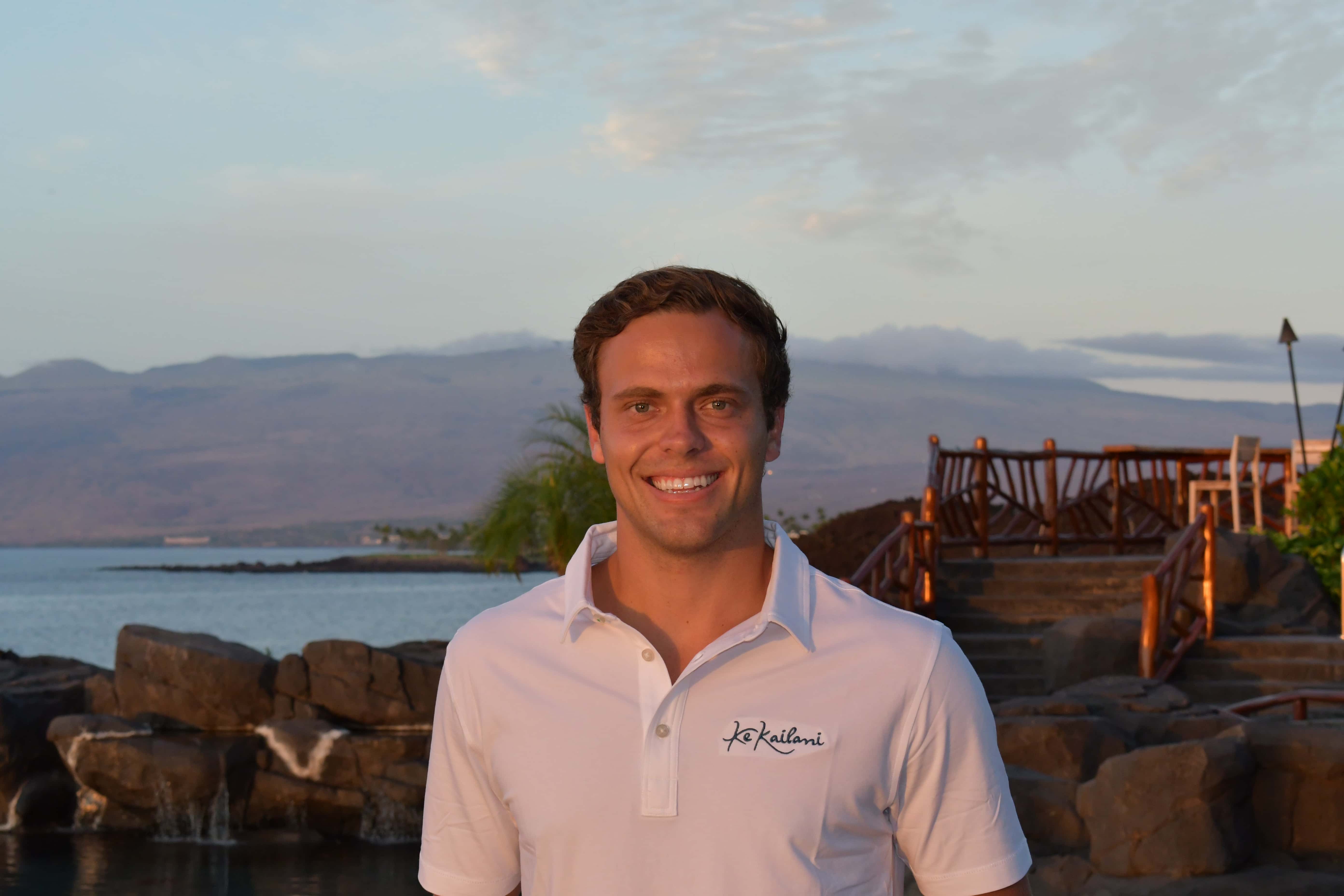 man in white shirt smiling with ocean in background